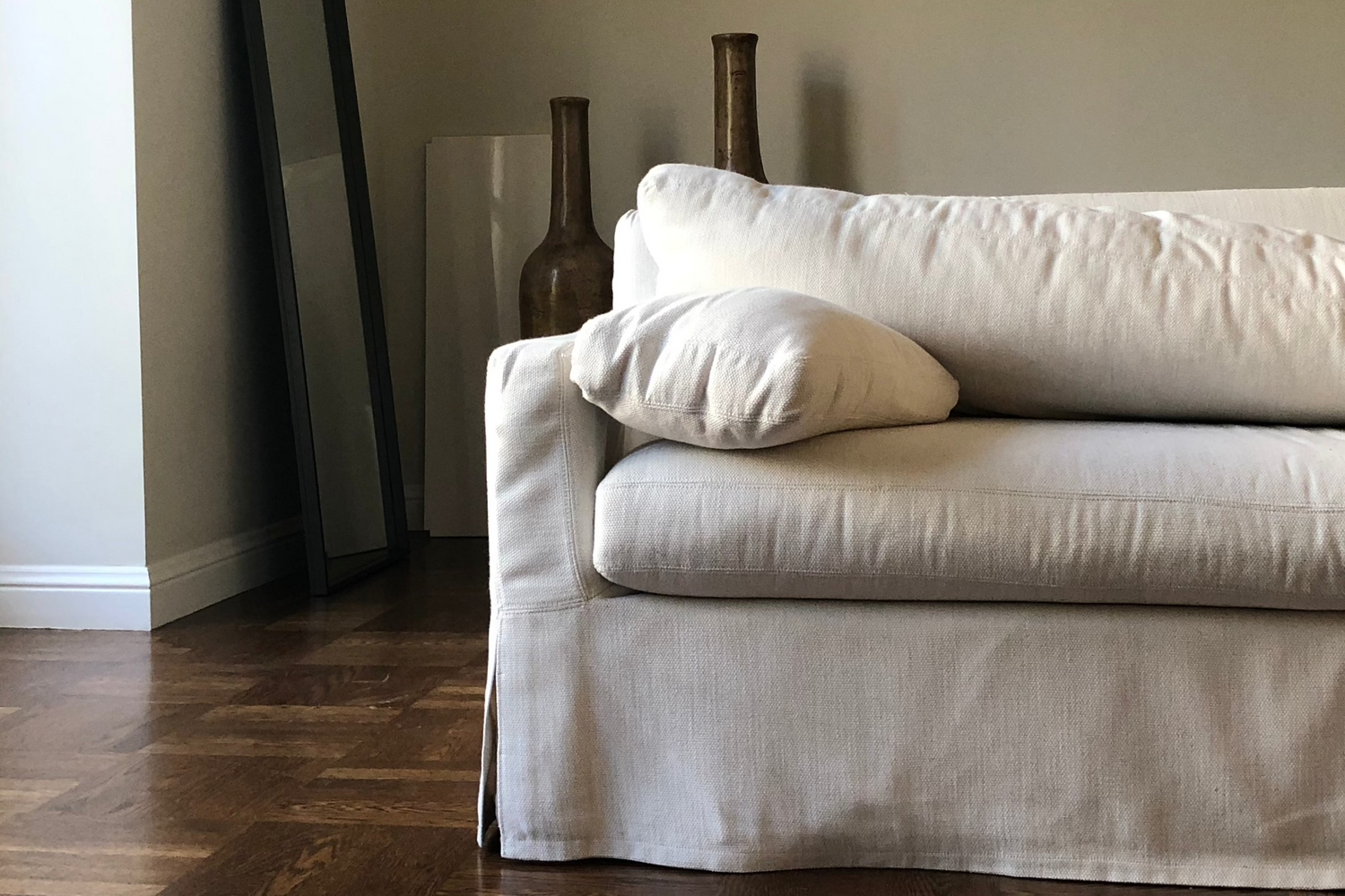 White sofa in a room with a mirror and decorative vases on a plain wall.